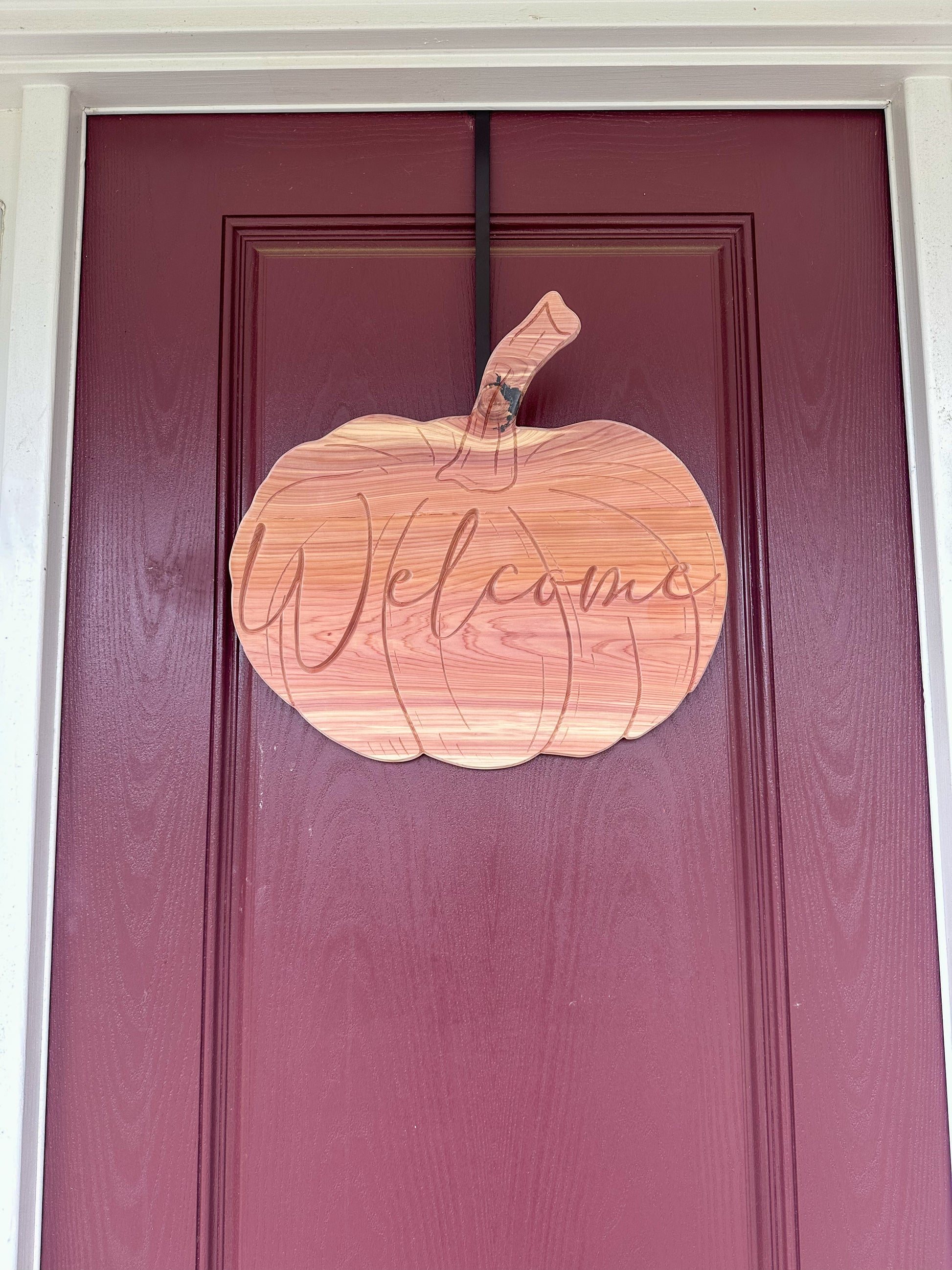 Wooden pumpkin-shaped 'Welcome' sign on a maroon door
